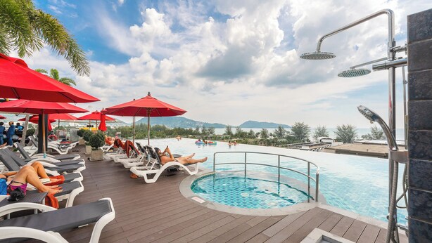 A poolside area with lounge chairs and red umbrellas, a hot tub, and a view of the sea. - 1BR with Pool 3 Min Walk to Beach  C197 (Patong)