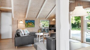 Ein modernes Wohnzimmer mit einer Couch, einem Esstisch und einer durchgehenden Tür erkennbaren Küchenzeile.