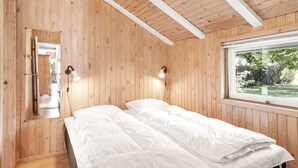 Ein Schlafzimmer mit Holzwänden, einem großen Fenster und einem Bett mit weißer Bettwäsche.