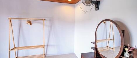 Een kamer met een houten plafond, een vloerventilator, een houten kast en een spiegel op een houten dressoir.