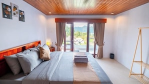 A bedroom with a wooden ceiling, a bed with grey and beige bedding, a nightstand, and a view of mountains through large windows. - Royal Escape (Kintamani)