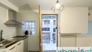 A kitchen with white cabinets, a stainless steel sink, patterned floor tiles, a hanging light fixture, and a view of a brick wall through an open door.