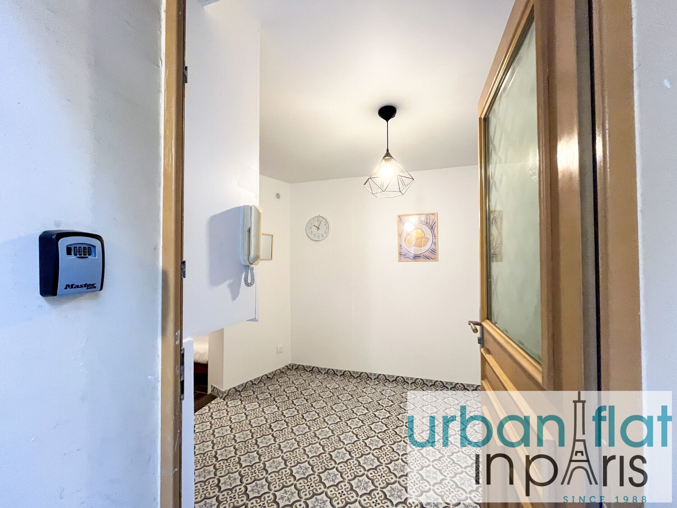 Un couloir avec un revêtement de sol à motifs, un téléphone fixé au mur, une horloge et un luminaire suspendu.