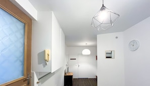 Un couloir avec un revêtement de sol à motifs, un téléphone fixé au mur, un luminaire suspendu et une horloge.