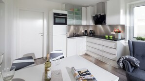 A modern kitchen with white cabinets, a black countertop, and a dining area with a table set for two. - // HOUSE DEICHBLICK - APARTMENT 1 // (Norderney)