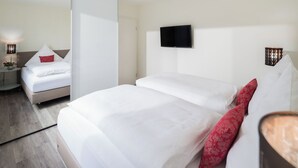 A hotel room with two beds, a flat-screen TV mounted on the wall, and a bedside table with a lamp. - // HOUSE DEICHBLICK - APARTMENT 1 // (Norderney)