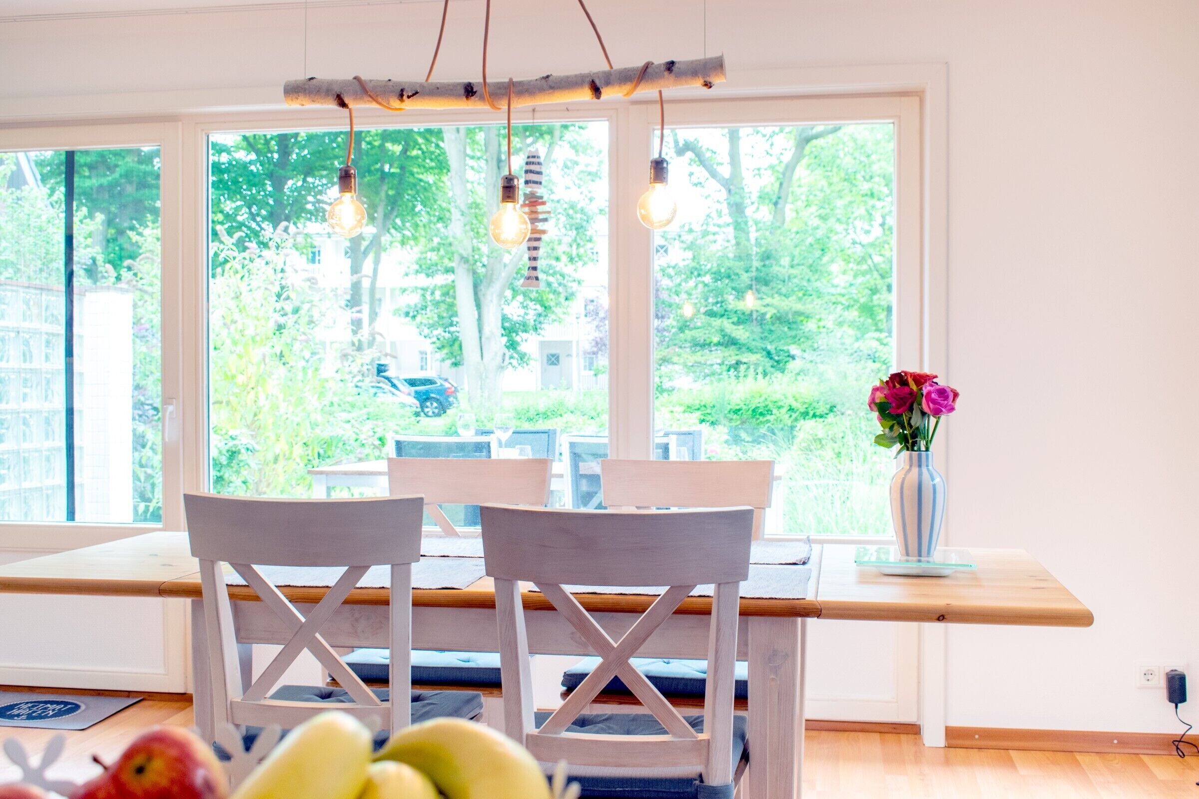 Ein Essbereich mit Holztisch und -stühlen, einer Blumenvase und Blick ins Grüne.