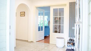 A hallway with a tiled floor, a white door, a bookshelf, and a shoe rack.