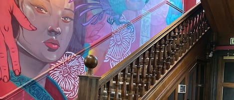A staircase with a colorful mural, a yellow tufted sofa, and a small table with a candle.