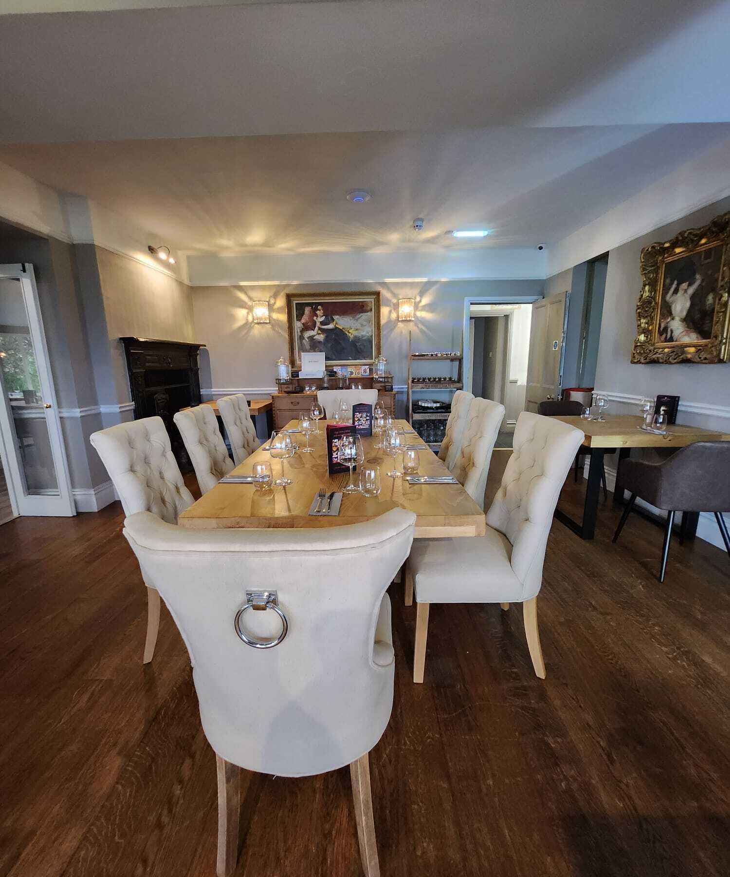 A dining area with a long wooden table set for six, surrounded by upholstered chairs with metal rings.