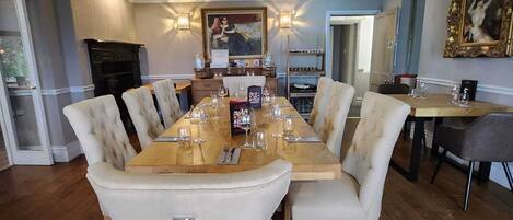 A dining area with a long wooden table set for six, surrounded by upholstered chairs with metal rings.