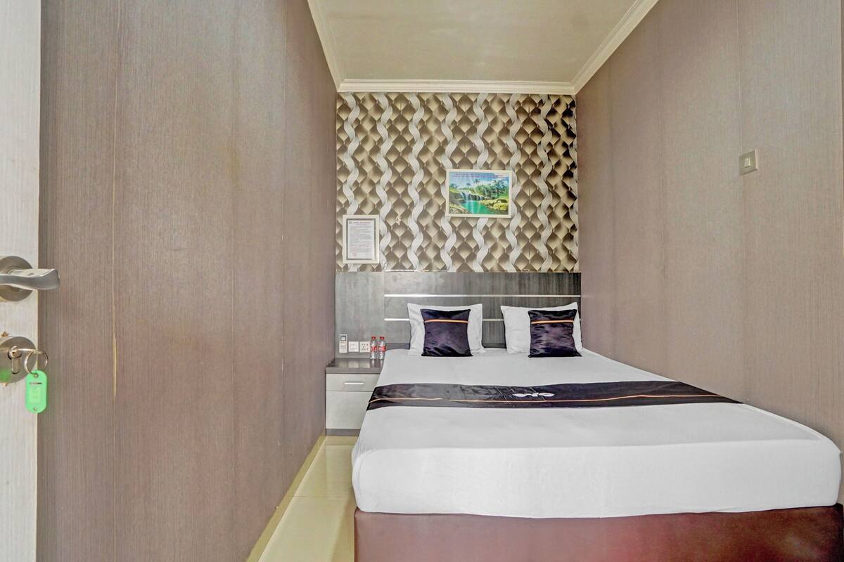 A hotel room with a bed, a nightstand, a mirror, and a wall with a patterned design.