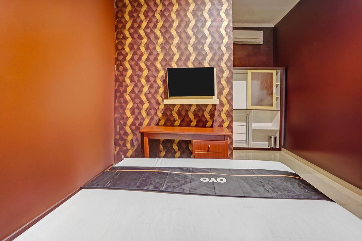 A hotel room with a bed, a desk, and a television mounted on the wall.