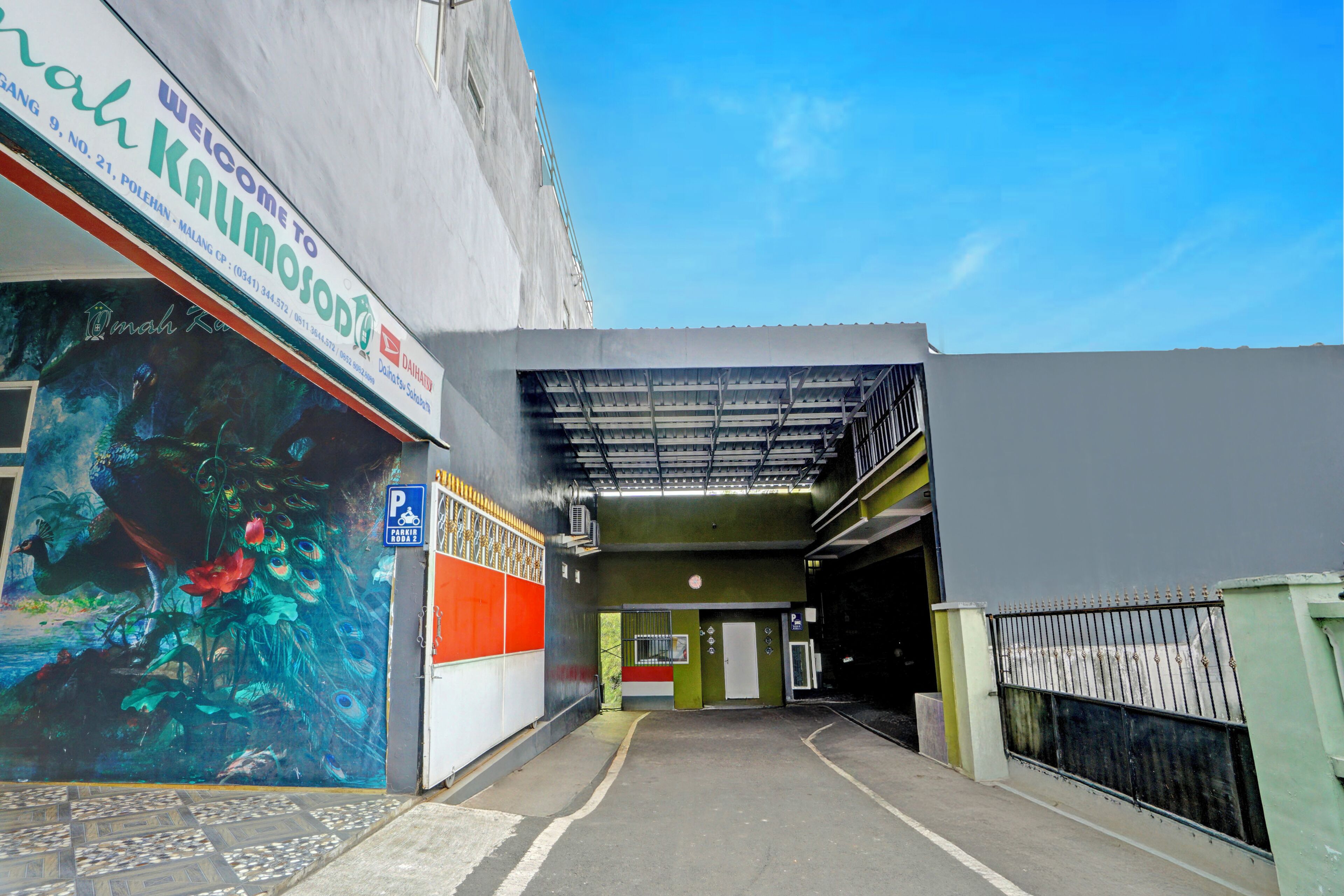 A parking garage entrance with a mural on the left wall, a covered walkway, and a gated area to the right.