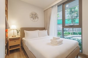 Habitación de hotel con cama, mesita de noche con lámpara, decoración en la pared y vistas al exterior con vegetación.