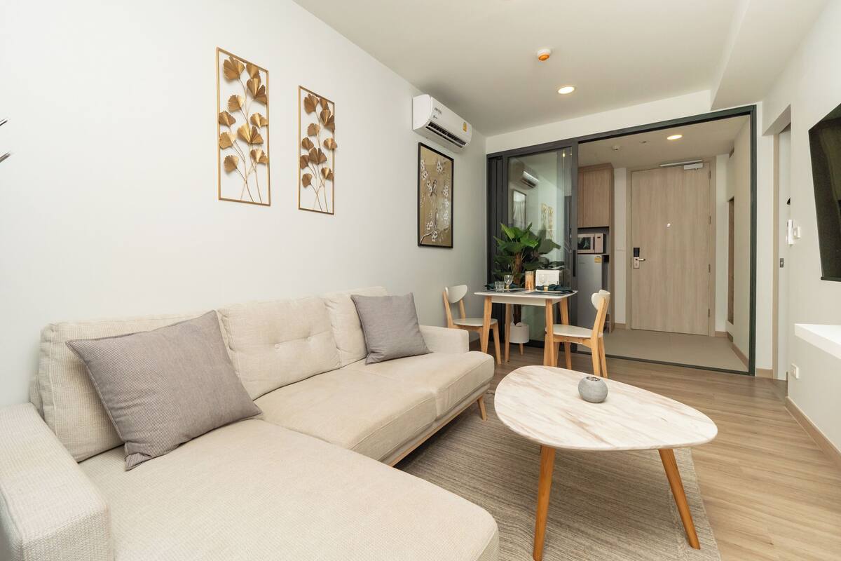 Una sala de estar moderna con un sofá beige, una mesita redonda y un comedor con una pequeña mesa y sillas.