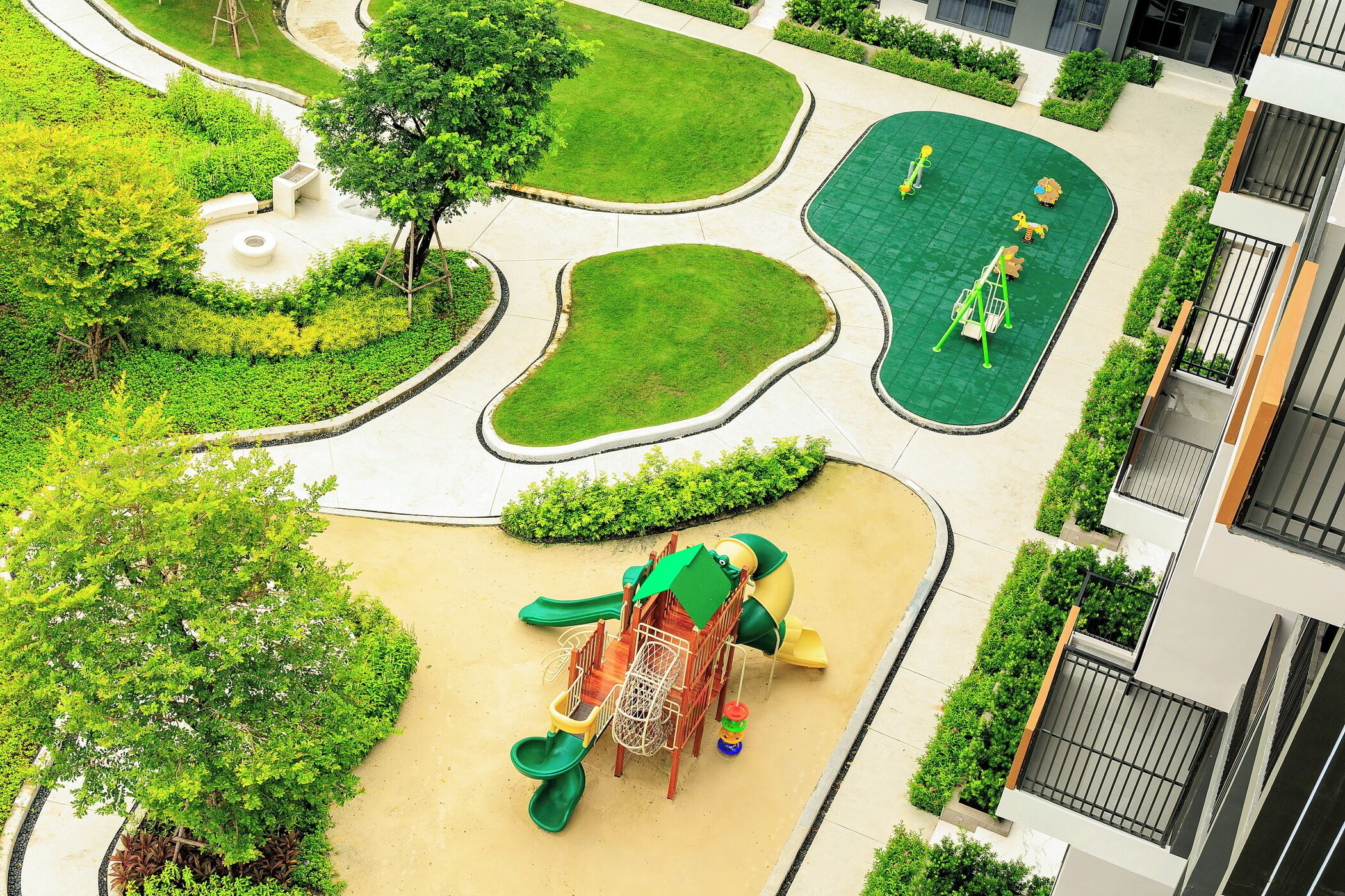 A playground with a slide, swings, and a climbing structure surrounded by landscaped areas and a building with balconies.