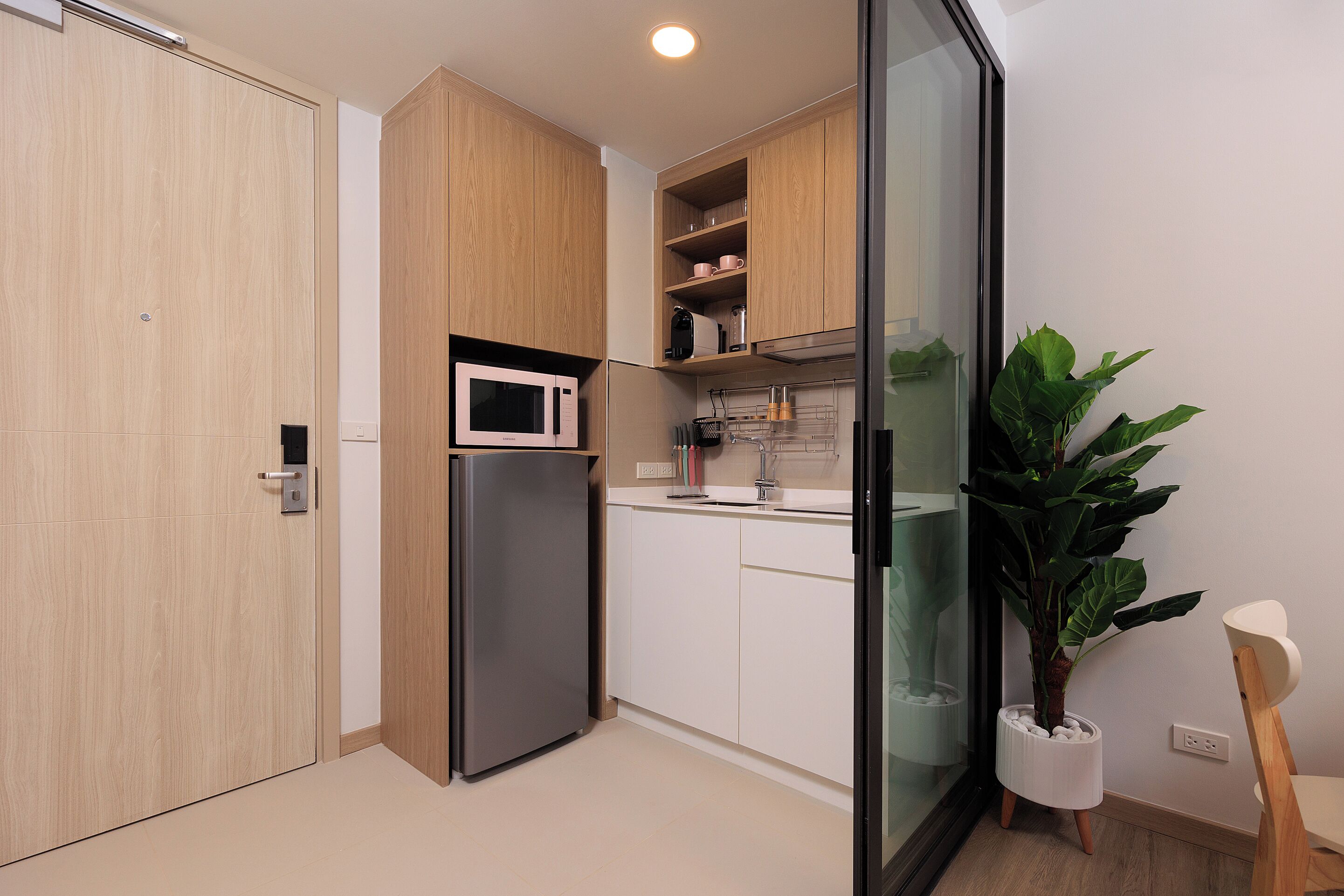 A modern kitchen with wooden cabinets, a stainless steel refrigerator, a microwave, and a potted plant.