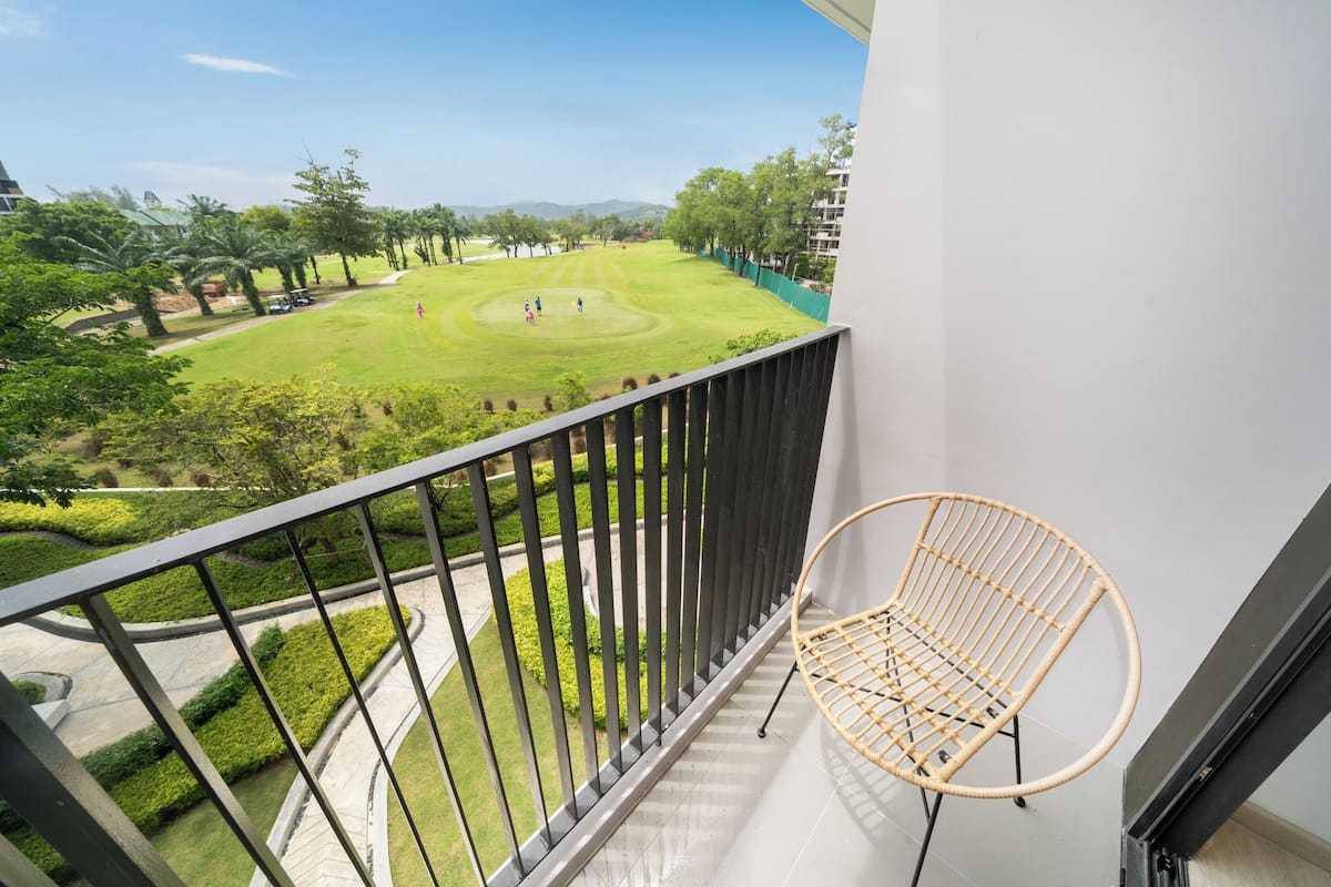 Un balcón con vistas a un campo de golf, una silla de mimbre y una pared blanca.