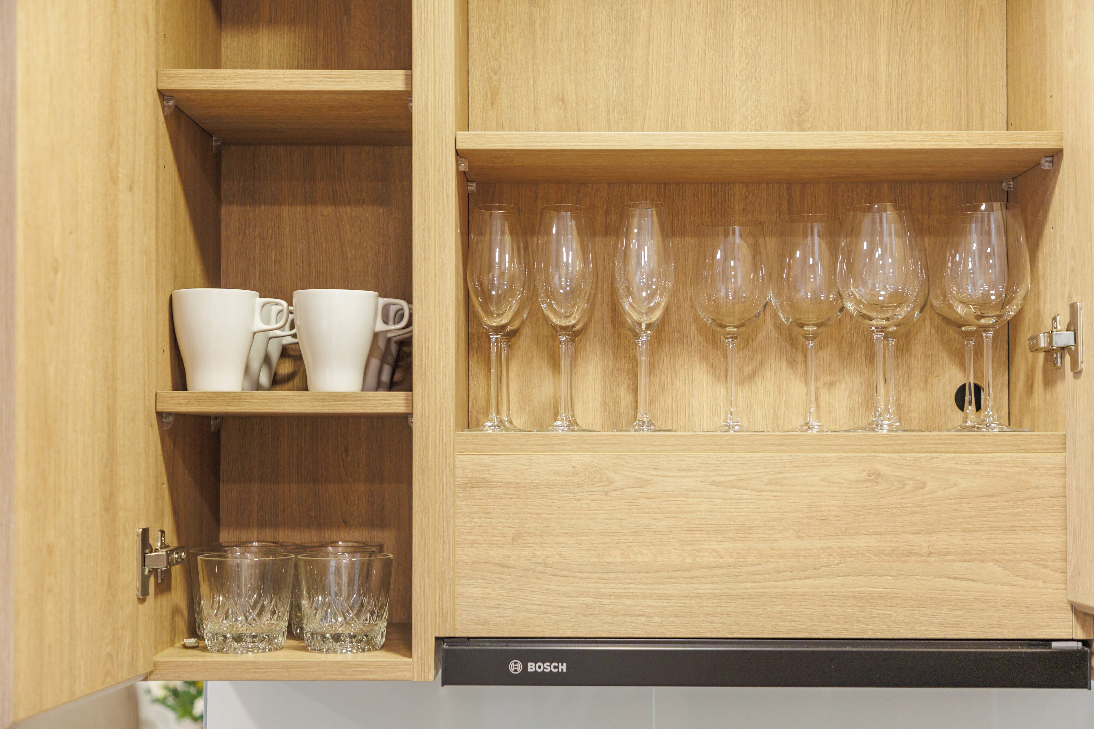 A wooden cabinet with shelves holding white cups and wine glasses.