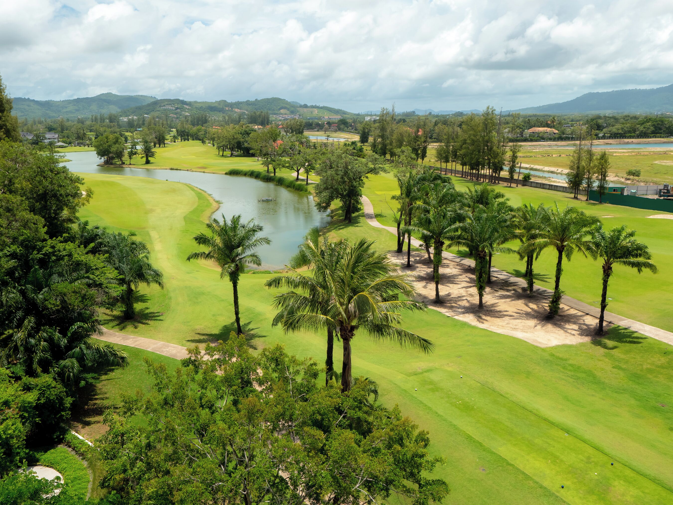 A golf course with a pond, palm trees, and a view of distant hills.