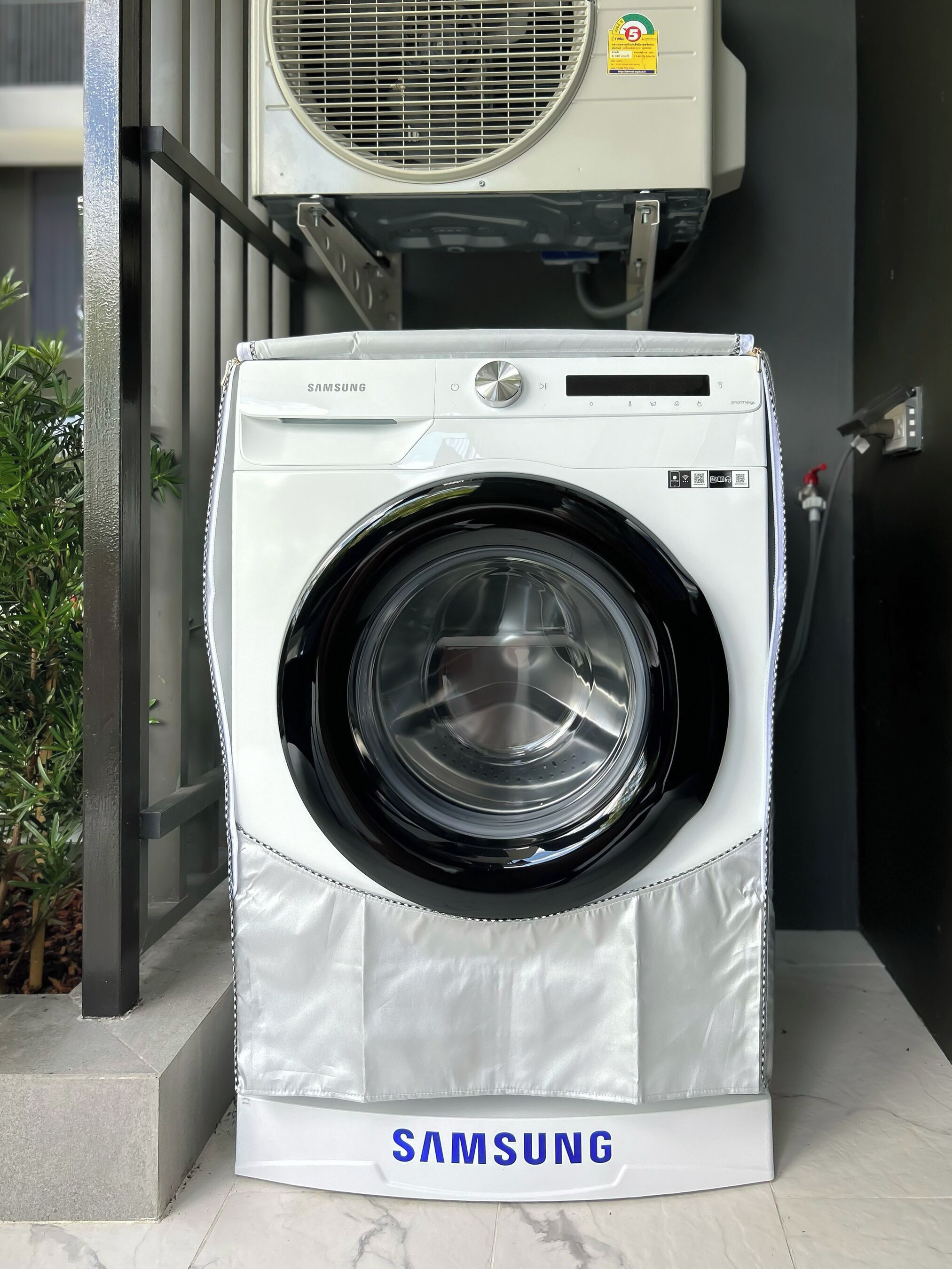 A Samsung front-loading washing machine with a stainless steel door, placed on a tiled floor.