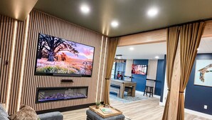 A modern living room with a flat-screen TV, a fireplace, and a dining area in the background. - Mallards Nest on Lay Lake: Game Room & Boat Ramp (Shelby)