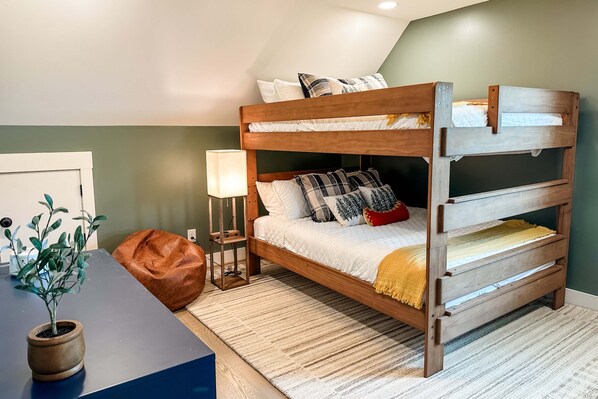 A bunk bed with a wooden frame, a bedside table with a lamp, a potted plant, and a brown bean bag chair.