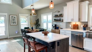 A modern kitchen with white cabinets, a stainless steel dishwasher, and a central island with bar stools. - Mallards Nest on Lay Lake: Game Room & Boat Ramp (Shelby)