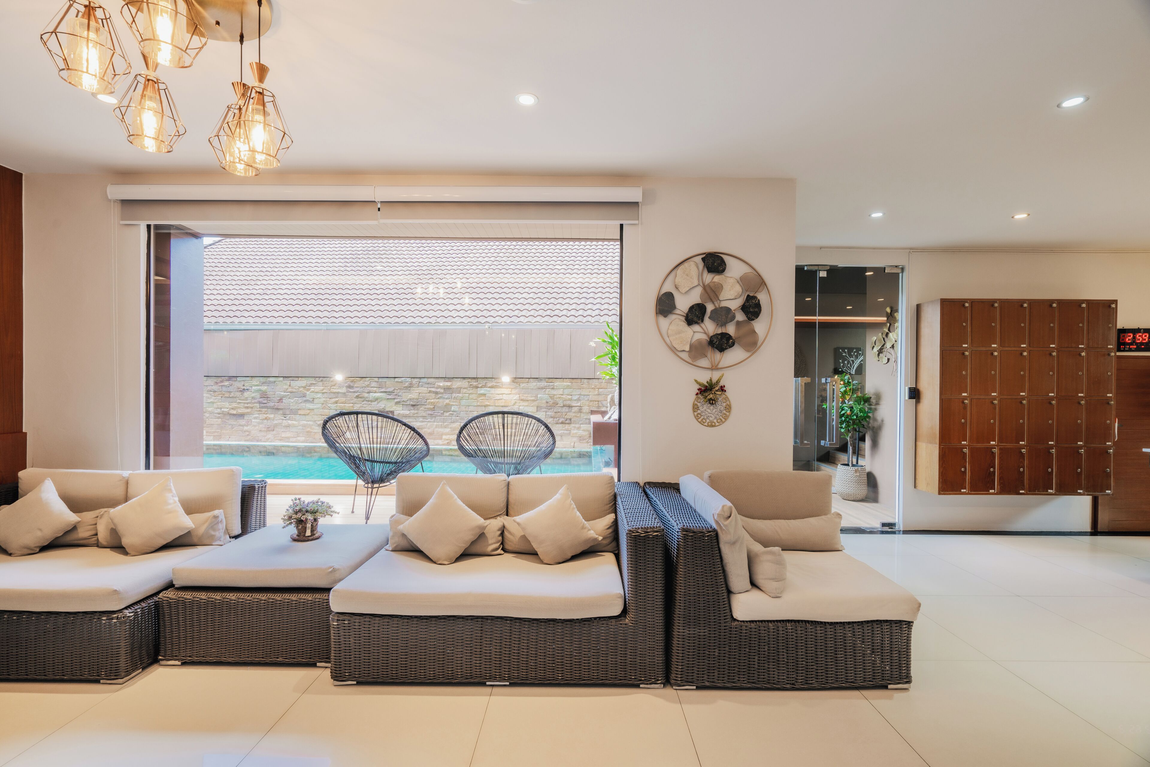 A modern living room with a sectional sofa, a dining area with chairs, a wall-mounted clock, and a view of the outdoors.