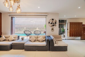 A modern living room with a sectional sofa, a dining area with chairs, a wall-mounted clock, and a view of the outdoors. - Westkey Kamala Hotel (Kamala)