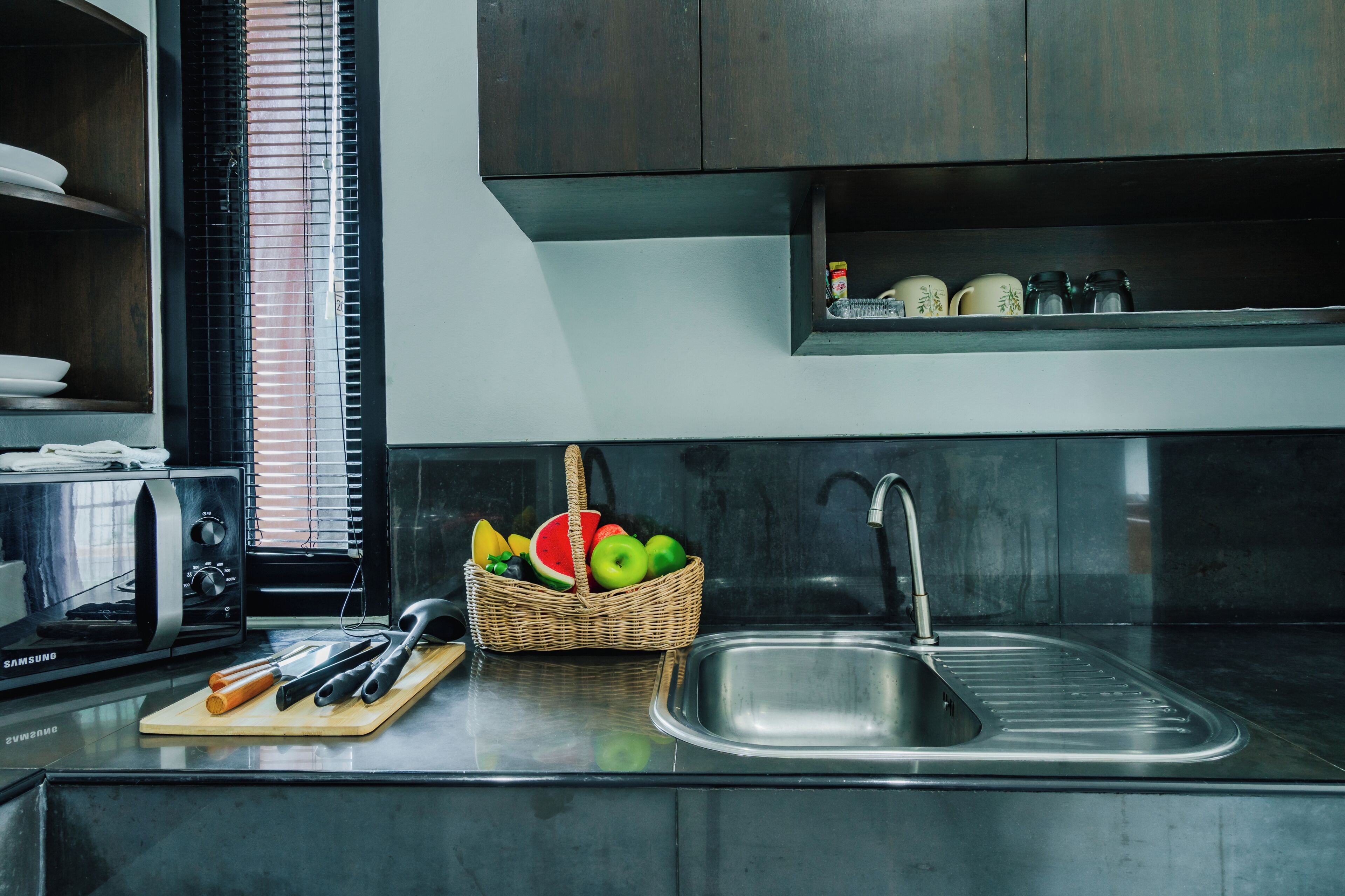 Una cocina con microondas, tostadora, fregadero y una cesta de frutas.
