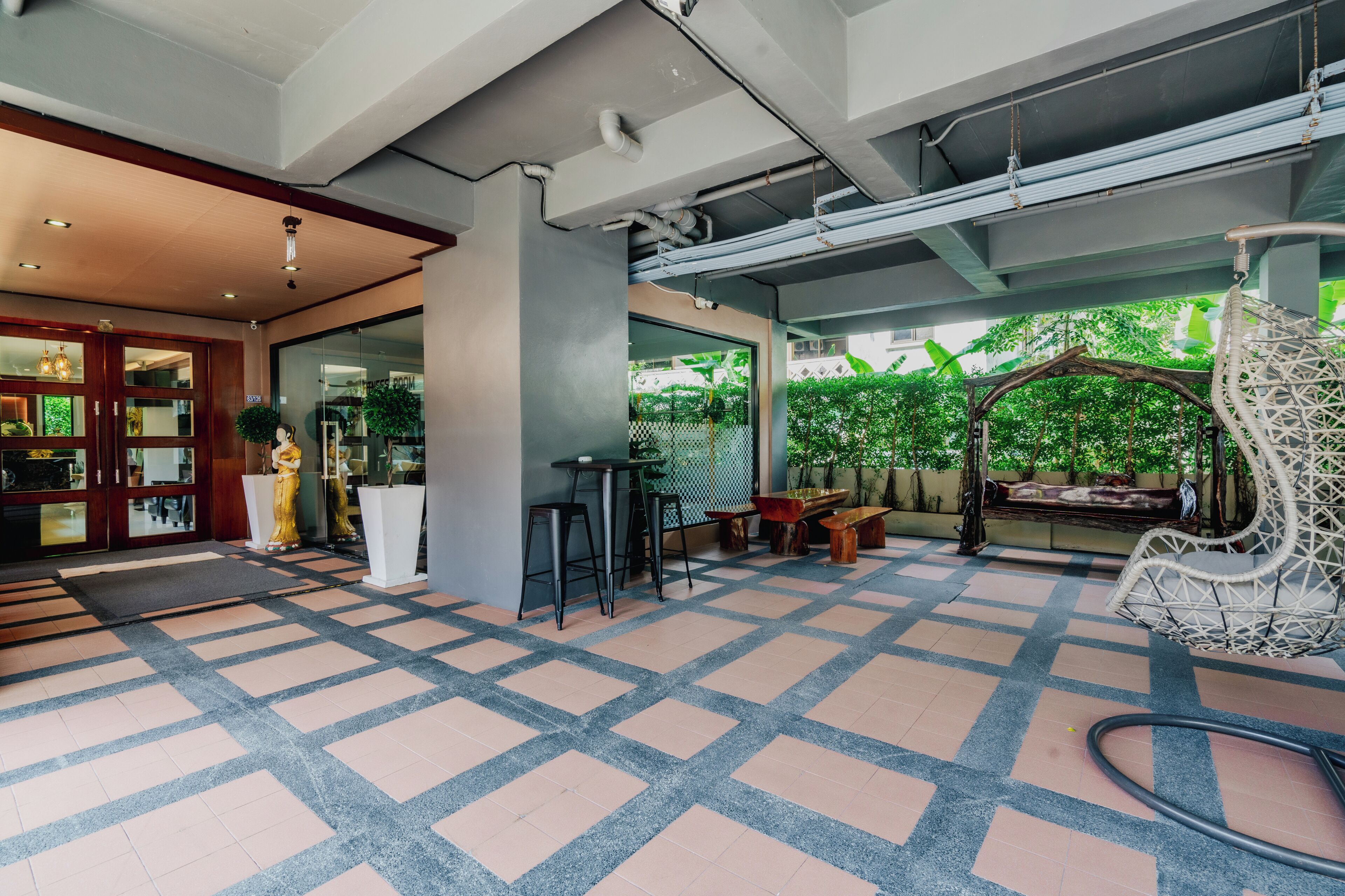 A modern indoor space with a checkered floor, a seating area with a swing chair, and a view of greenery outside.