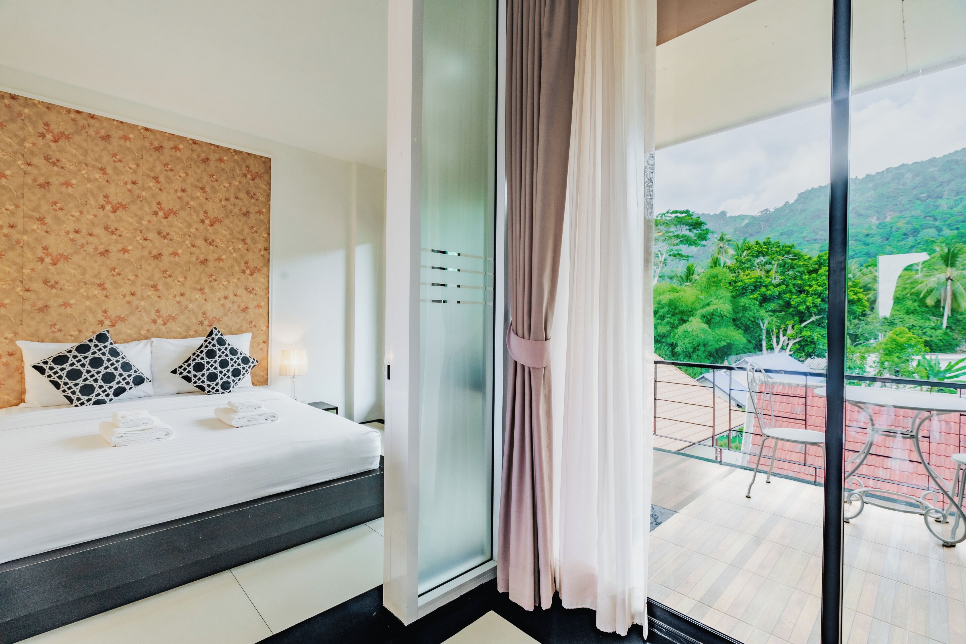 Ein Hotelzimmer mit einem Bett, einer Glastür, die auf einen Balkon führt, und Blick ins Grüne.
