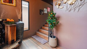 A staircase with a wooden finish, a large vase with orange flowers, and a wall-mounted picture frame. - Westkey Kamala Hotel (Kamala)