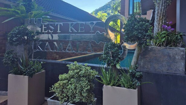 A sign for 'WEST KEY KAMALA' with a pool and potted plants in the foreground. - Westkey Kamala Hotel (Kamala)