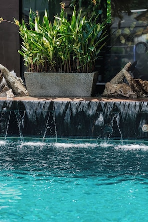 A pool with clear water, a planter with green plants, and a stone ledge. - Westkey Kamala Hotel (Kamala)