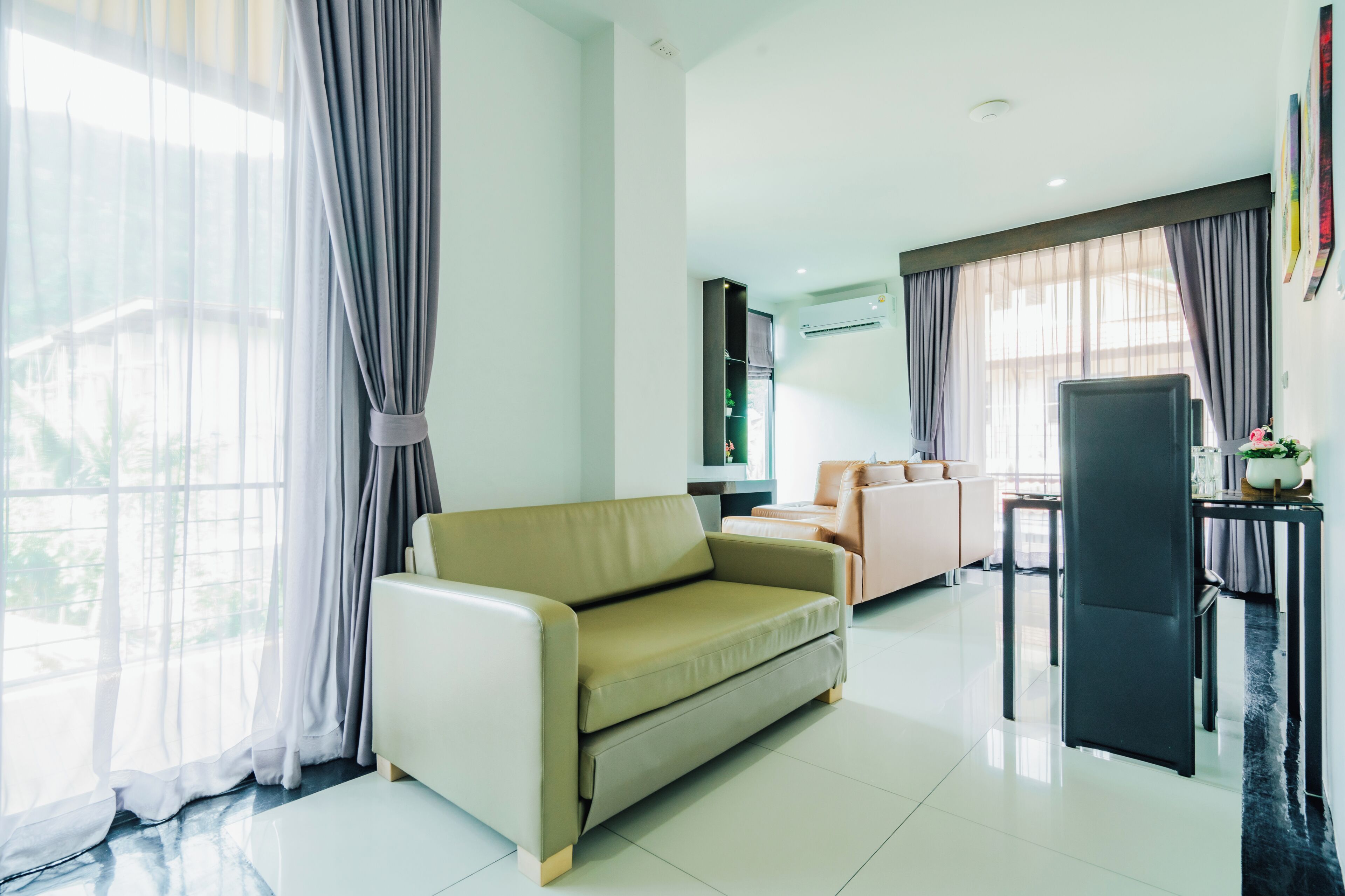 A modern living room with a sofa, a TV, a dining area, and a large window with curtains.