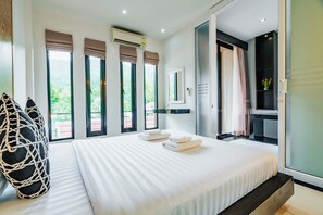 Una habitación de hotel moderna con una cama grande, un rincón de descanso con una silla de mimbre y vistas a zonas verdes a través de las ventanas.