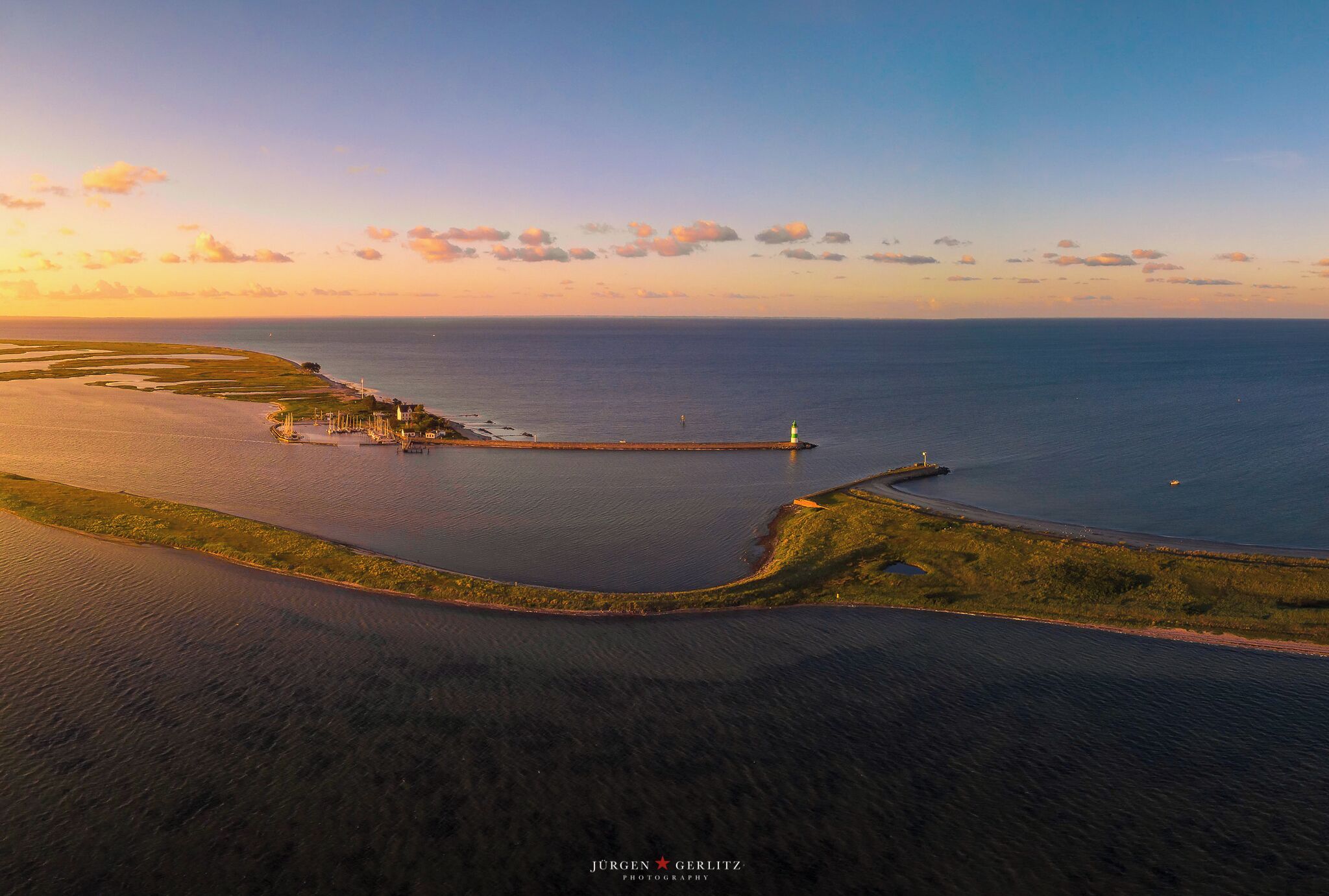 Vista aérea de una zona costera con un faro, un rompeolas y un puerto deportivo.