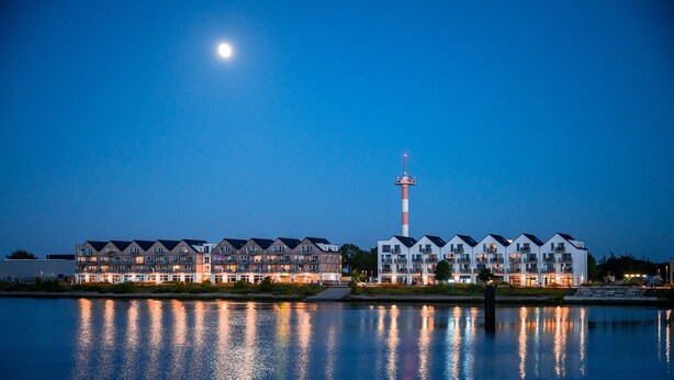 Un hotel frente al agua con edificios de varios pisos, un faro destacado y reflejos en el agua.