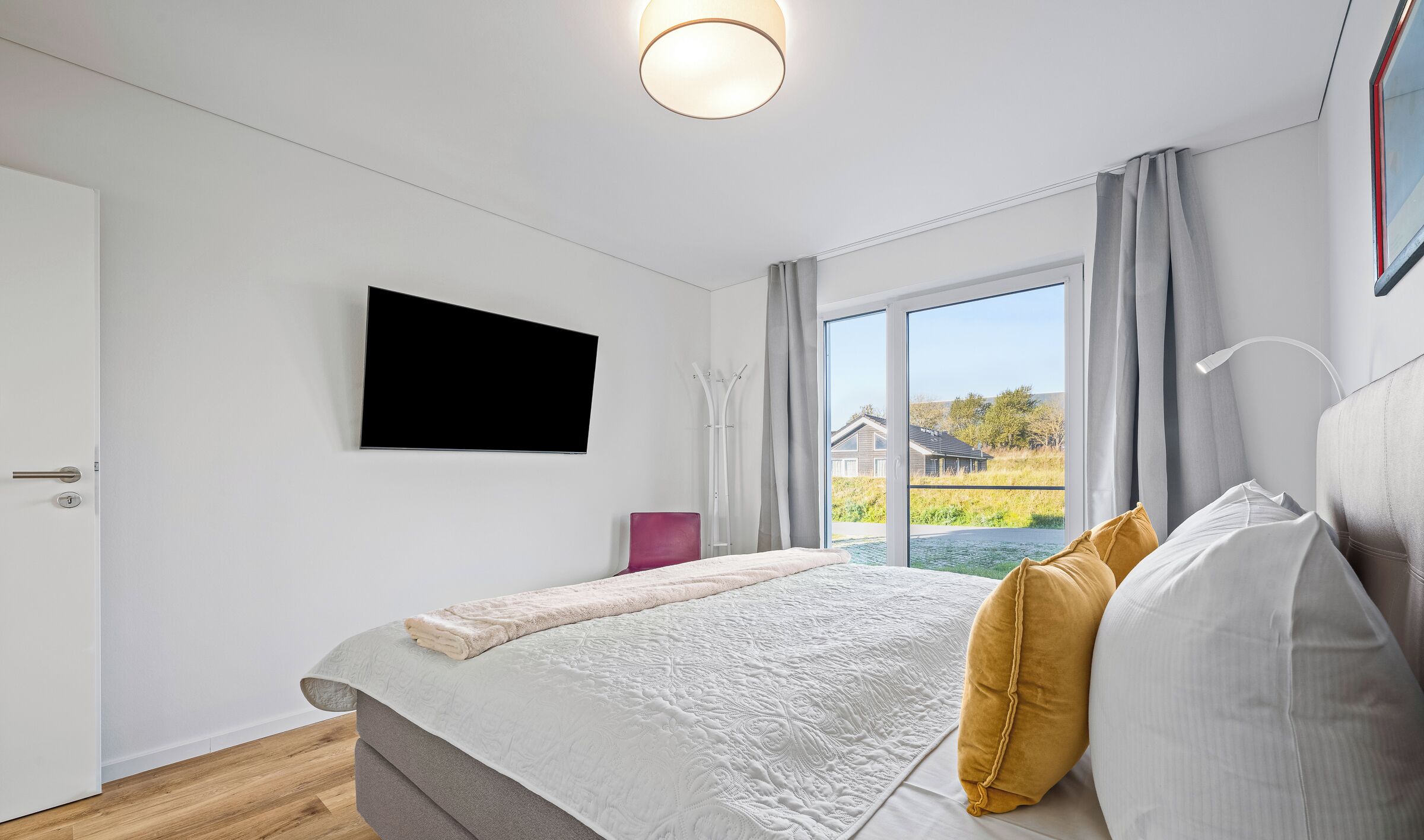 Un dormitorio moderno con una cama grande, un televisor de pantalla plana en la pared y un ventanal con cortinas.