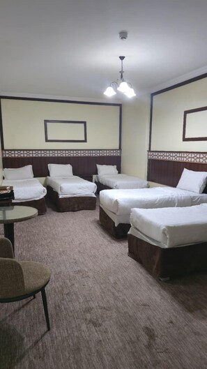 Una habitación de hotel con cuatro camas individuales, una mesita y una silla.