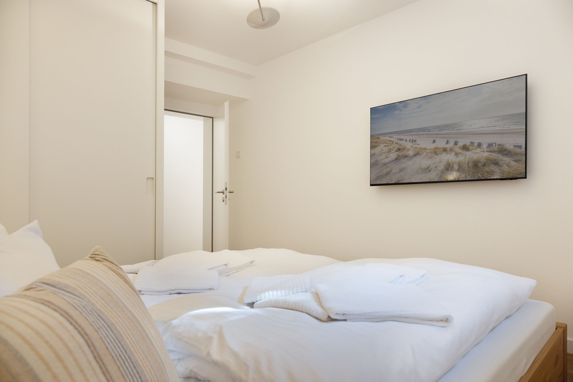 A bedroom with a bed, pillows, and a painting of a beach scene on the wall.