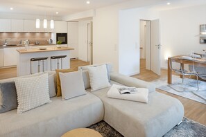 A modern living room with a sofa, a dining table with chairs, and a kitchen area with bar stools. - Welcome to the Cap Alma apartment (List)