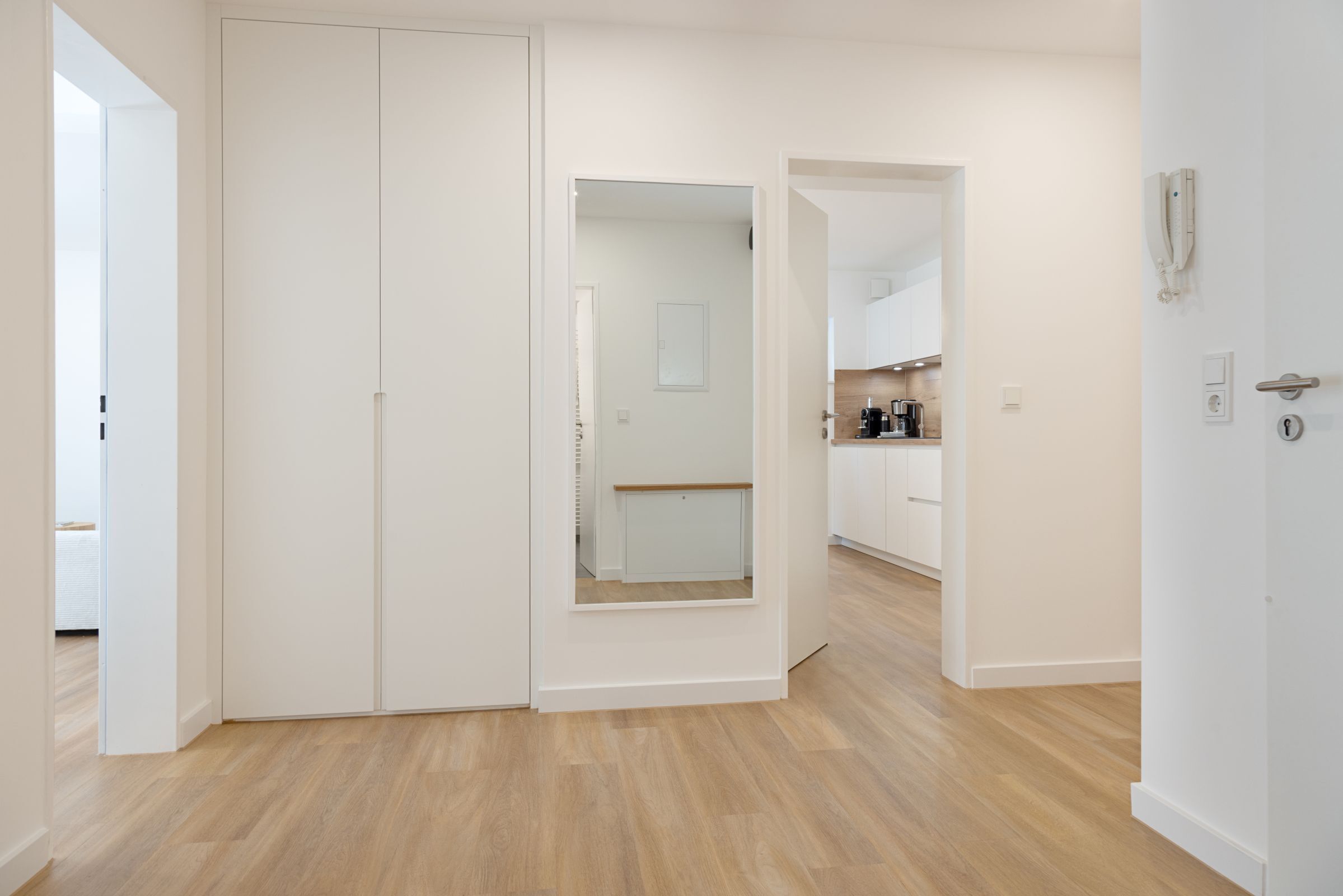 A modern, minimalist room with a wooden floor, white walls, and a large wardrobe.