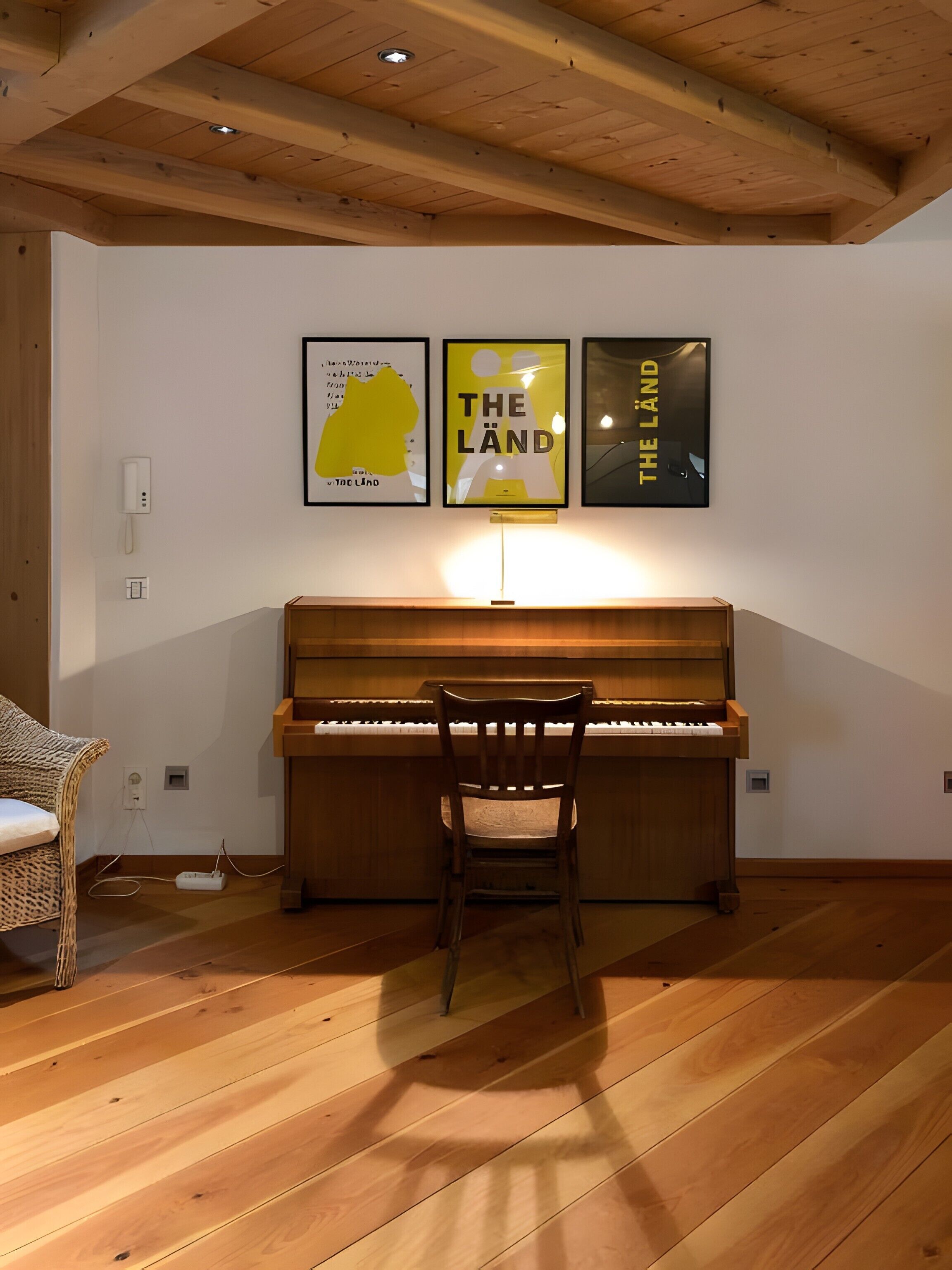 Un piano con una silla frente a él, una pared con obras de arte enmarcadas y un techo de madera.