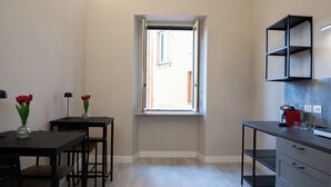 Una cocina pequeña y luminosa con ventana, una mesa de comedor con sillas y una cafetera.