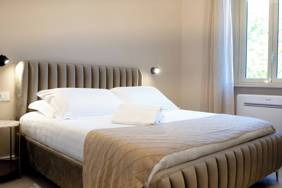 Una cama bien hecha con cabecera, mesita de noche y una silla.