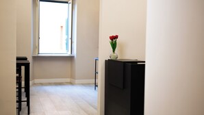 Un pasillo con ventana, un armario negro y un jarrón con flores rojas.